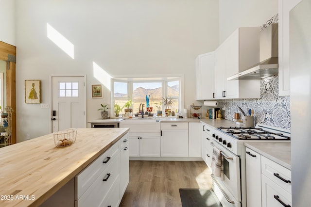 kitchen featuring backsplash, sink, wall chimney range hood, white cabinets, and white gas stove