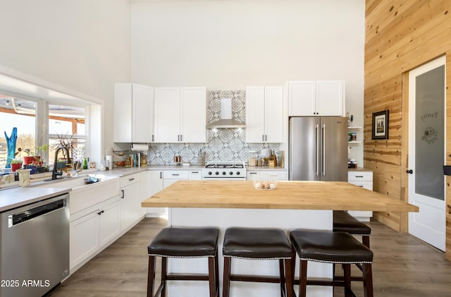 kitchen featuring white cabinets, a center island, stainless steel appliances, and wall chimney range hood