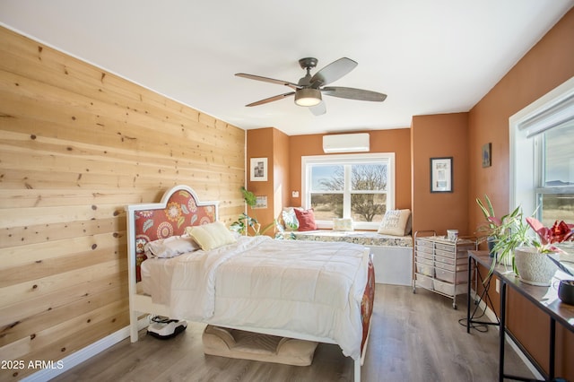 bedroom featuring a wall mounted air conditioner, dark hardwood / wood-style flooring, ceiling fan, and wood walls