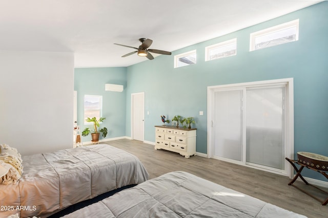 bedroom with a towering ceiling, light hardwood / wood-style flooring, ceiling fan, and an AC wall unit