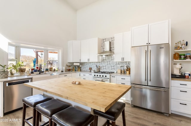 kitchen featuring appliances with stainless steel finishes, white cabinetry, and wall chimney range hood