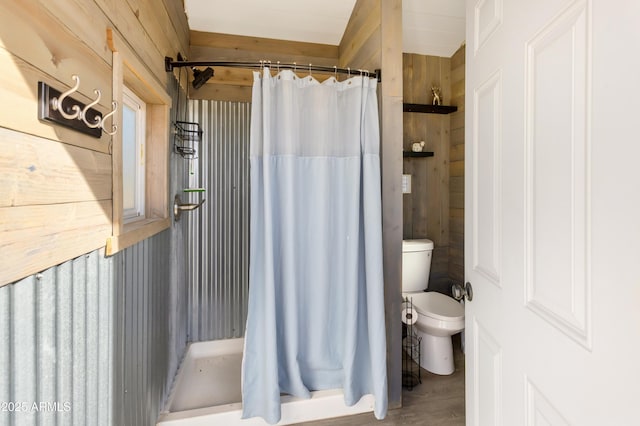 bathroom featuring a shower with curtain, toilet, and wooden walls