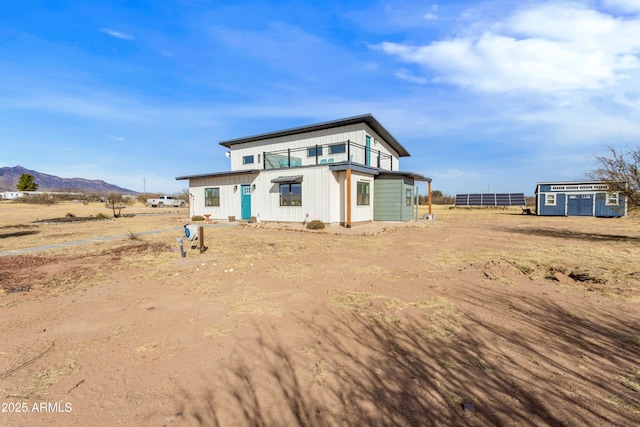 back of property featuring a mountain view, a balcony, and an outbuilding