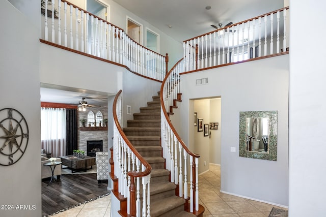 staircase with ceiling fan, a fireplace, a towering ceiling, and tile patterned floors