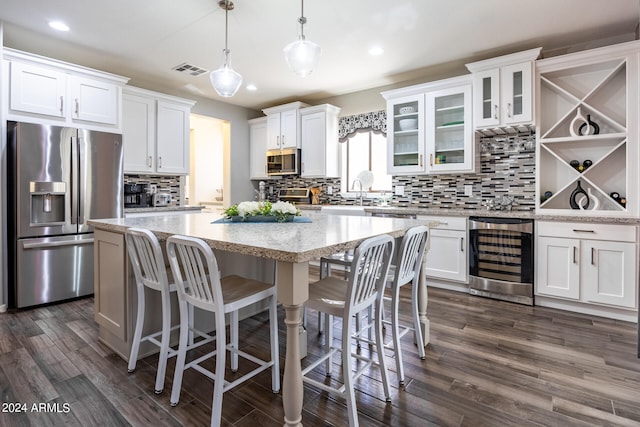 kitchen with white cabinets, hanging light fixtures, a kitchen island, beverage cooler, and appliances with stainless steel finishes