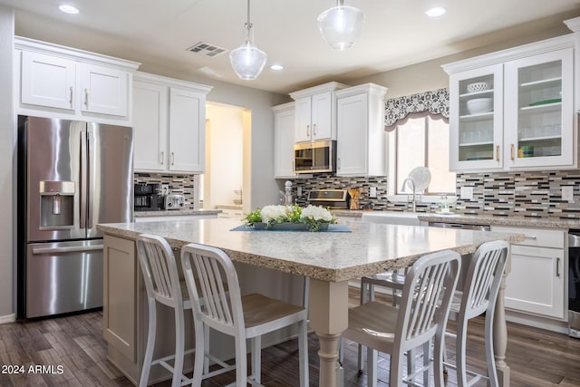 kitchen with white cabinets, appliances with stainless steel finishes, hanging light fixtures, and dark wood-type flooring