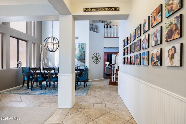 hallway with an inviting chandelier, a towering ceiling, and light tile patterned floors