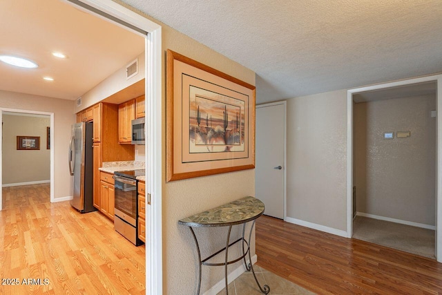 kitchen with a kitchen breakfast bar, stainless steel appliances, light stone countertops, light hardwood / wood-style floors, and a textured ceiling