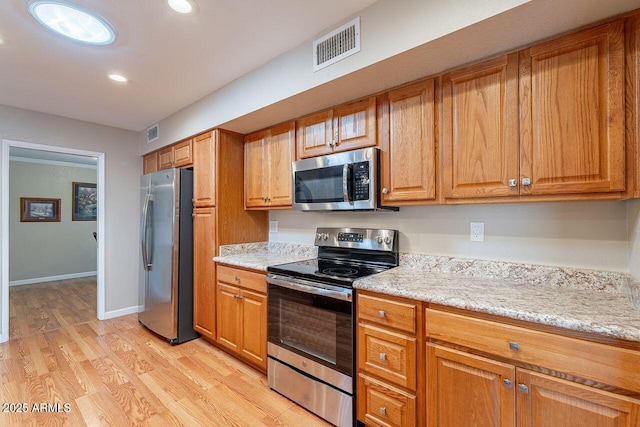 kitchen with light stone counters, appliances with stainless steel finishes, and light hardwood / wood-style floors