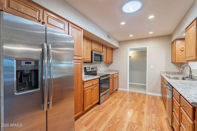 kitchen featuring light stone counters, appliances with stainless steel finishes, sink, and light hardwood / wood-style flooring