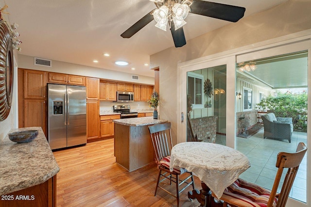 kitchen featuring light stone counters, stainless steel appliances, light hardwood / wood-style floors, and ceiling fan