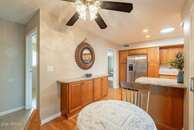 kitchen with stainless steel refrigerator with ice dispenser, light stone counters, and light wood-type flooring