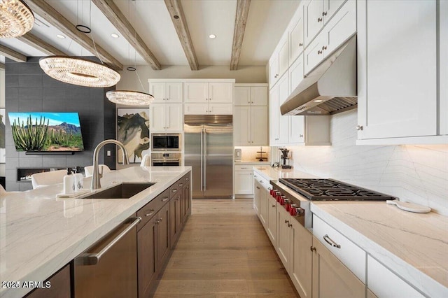 kitchen with decorative light fixtures, a sink, built in appliances, under cabinet range hood, and beam ceiling