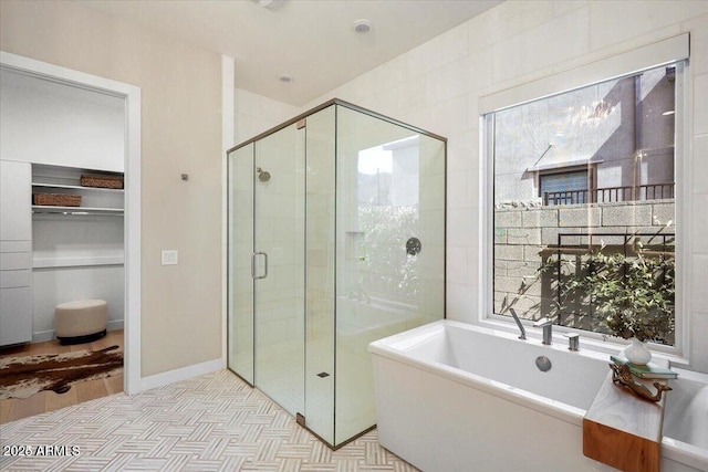 full bathroom featuring a closet, a freestanding tub, a shower stall, and baseboards