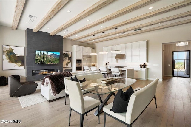 dining space with a large fireplace, beamed ceiling, light wood-type flooring, and visible vents