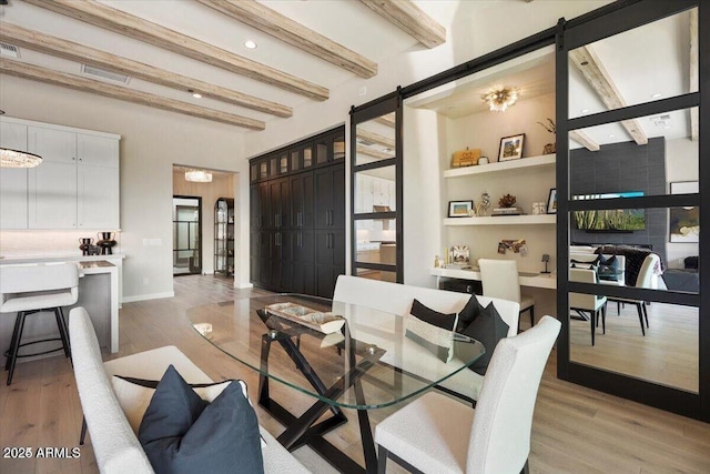 living room with beam ceiling, light wood finished floors, visible vents, a barn door, and baseboards