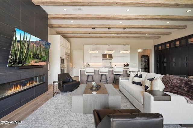 living room featuring visible vents, beamed ceiling, a tiled fireplace, and wood finished floors