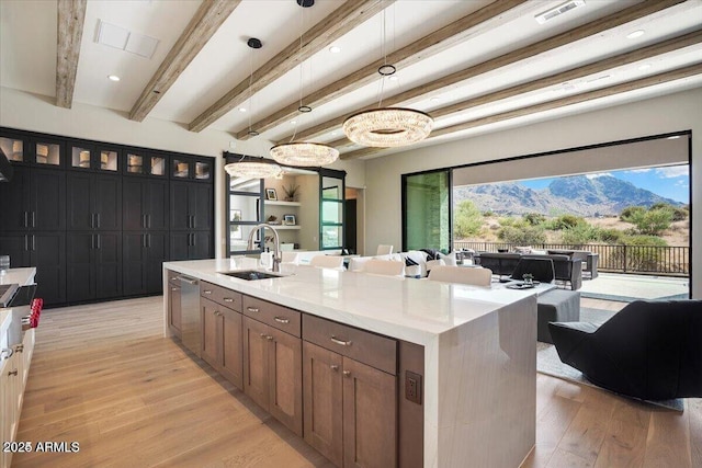 kitchen with a kitchen island with sink, a sink, hanging light fixtures, light countertops, and glass insert cabinets