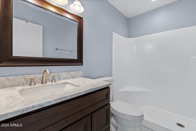 bathroom featuring vanity, walk in shower, and toilet