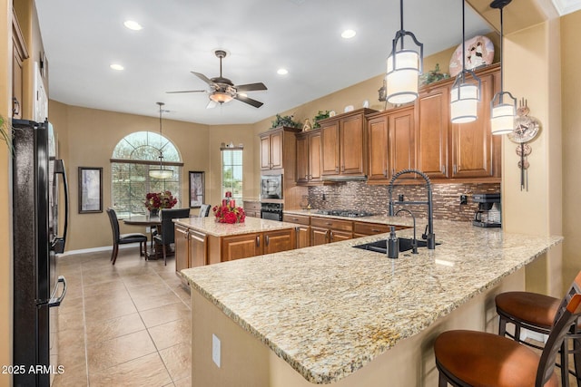 kitchen with kitchen peninsula, ceiling fan, pendant lighting, light stone counters, and black appliances