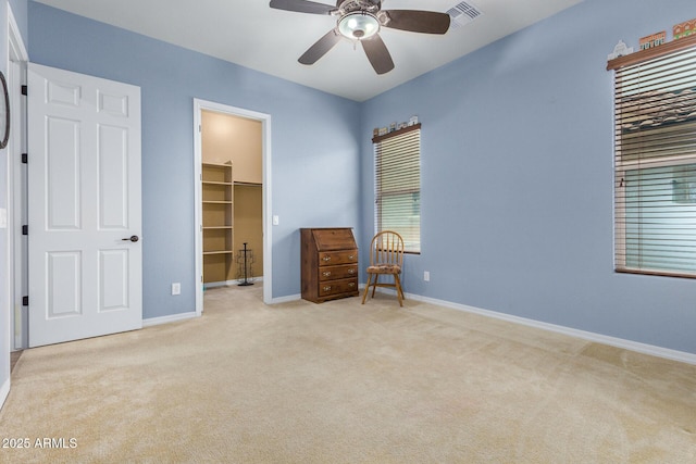 unfurnished bedroom with ceiling fan, a walk in closet, a closet, and light colored carpet