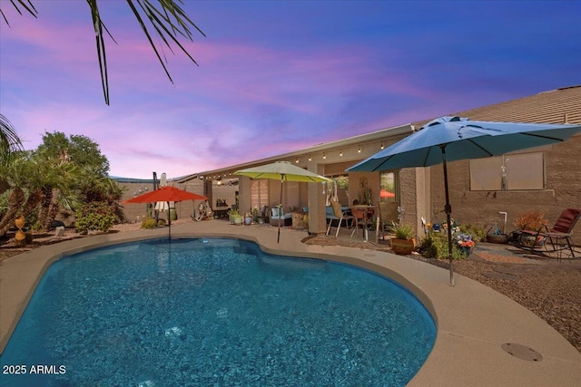 pool at dusk featuring an outdoor pool and a patio