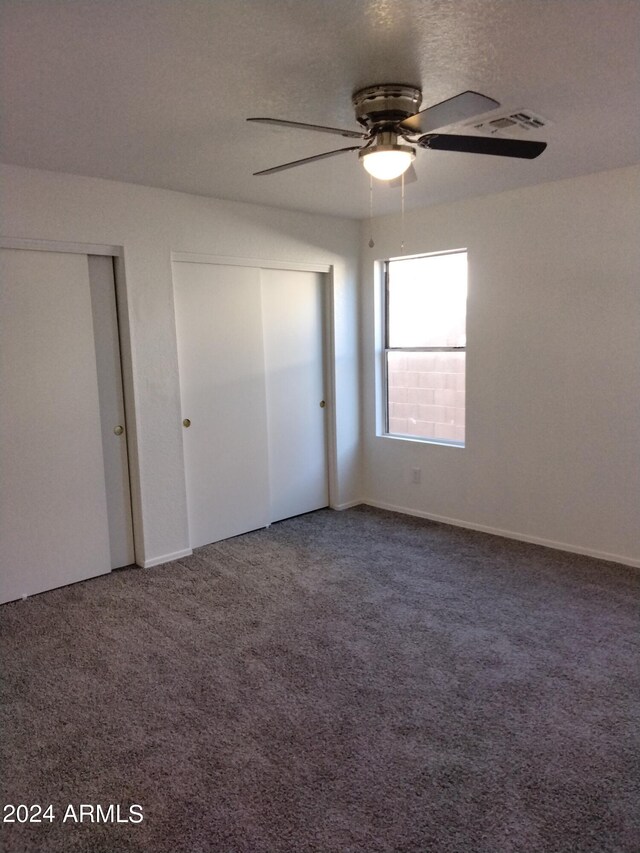 unfurnished bedroom featuring carpet floors, ceiling fan, and multiple closets