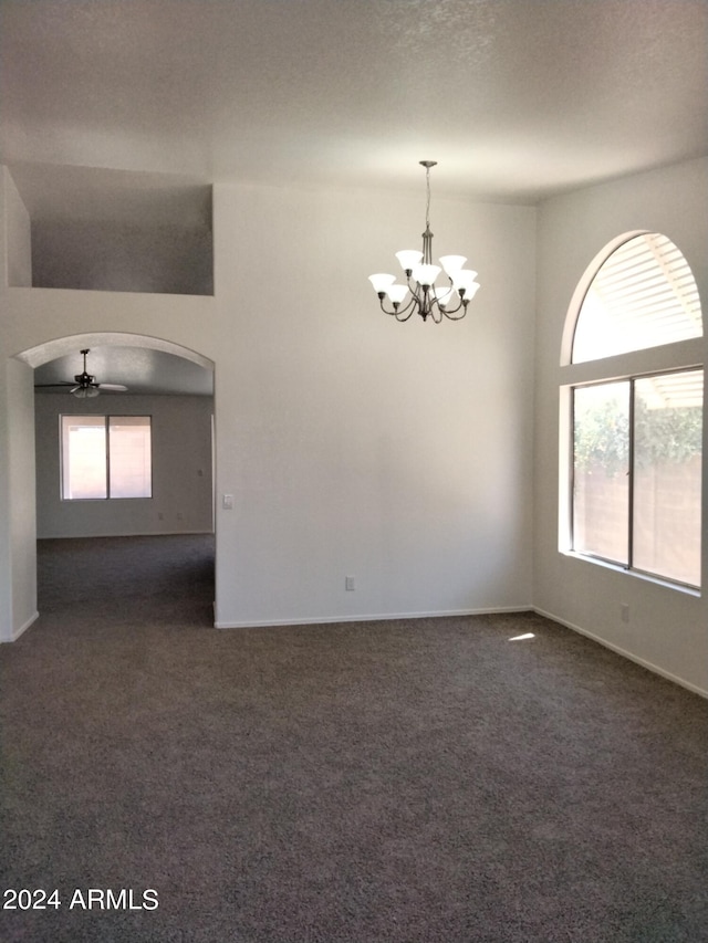 spare room featuring dark carpet and ceiling fan with notable chandelier