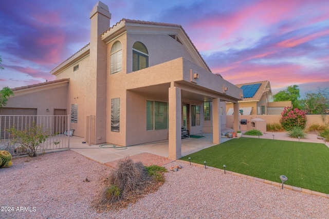 back house at dusk with a patio, a lawn, and solar panels