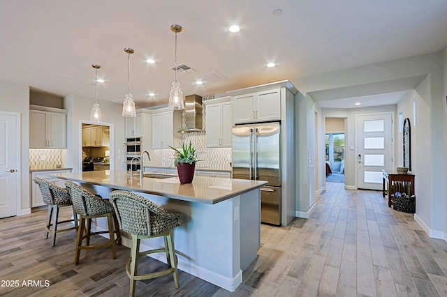kitchen featuring a sink, visible vents, appliances with stainless steel finishes, wall chimney range hood, and a center island with sink