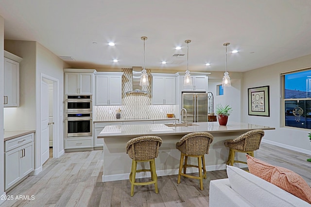 kitchen with a center island with sink, decorative backsplash, wall chimney exhaust hood, stainless steel appliances, and a kitchen bar