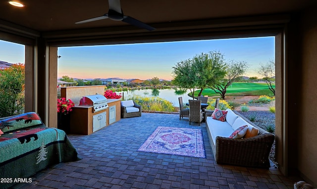 patio terrace at dusk featuring ceiling fan, area for grilling, a water view, an outdoor living space, and grilling area