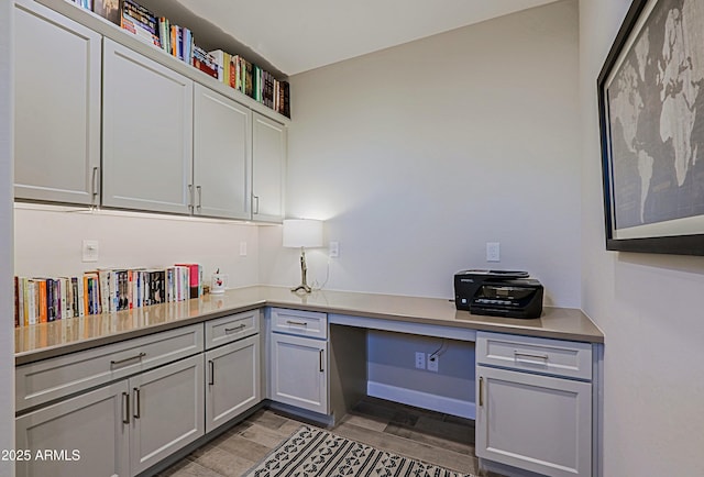 office area with baseboards, built in desk, and light wood-style floors