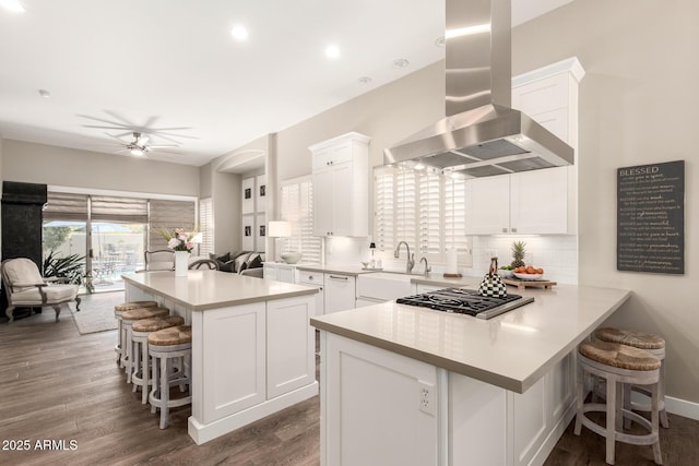 kitchen featuring a sink, wall chimney exhaust hood, white cabinetry, stainless steel gas stovetop, and a kitchen bar