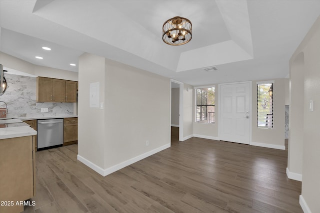 kitchen featuring tasteful backsplash, dishwasher, wood-type flooring, a chandelier, and a tray ceiling