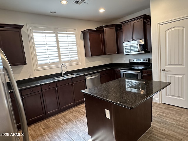 kitchen featuring a kitchen island, sink, dark stone countertops, light hardwood / wood-style floors, and stainless steel appliances