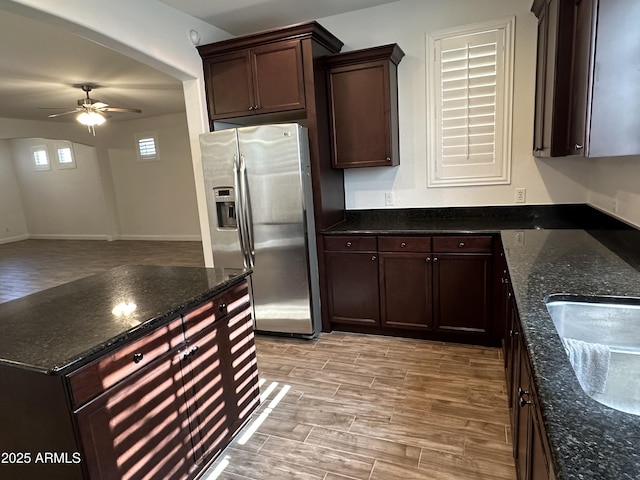 kitchen featuring dark stone countertops, light wood-type flooring, ceiling fan, and stainless steel refrigerator with ice dispenser