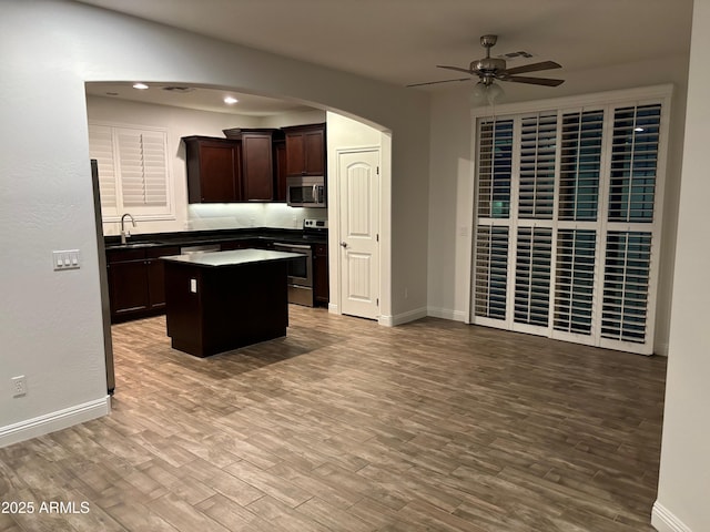 kitchen with appliances with stainless steel finishes, sink, a center island, dark brown cabinets, and light hardwood / wood-style flooring