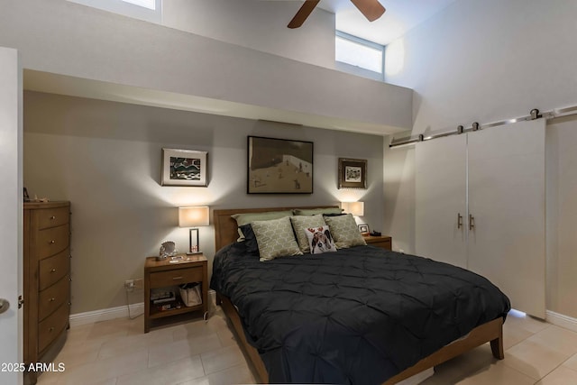 bedroom featuring light tile patterned floors, a barn door, a high ceiling, and baseboards