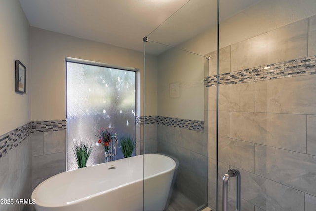 full bath featuring a wainscoted wall, tile walls, a tile shower, and a freestanding bath