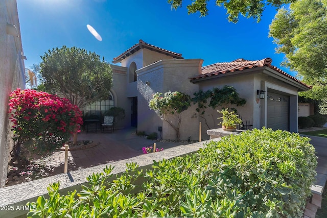 view of front of home featuring an attached garage, a patio area, a tile roof, and stucco siding