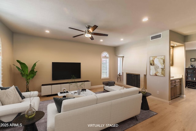 living area with recessed lighting, visible vents, a fireplace with raised hearth, light wood-style flooring, and baseboards