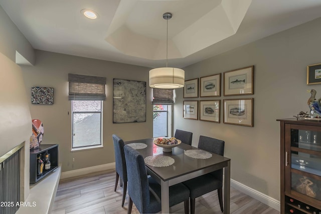 dining area featuring light wood-style floors, a tray ceiling, baseboards, and wine cooler