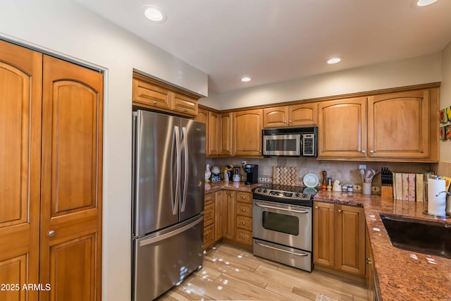 kitchen with decorative backsplash, dark stone counters, brown cabinets, stainless steel appliances, and a sink