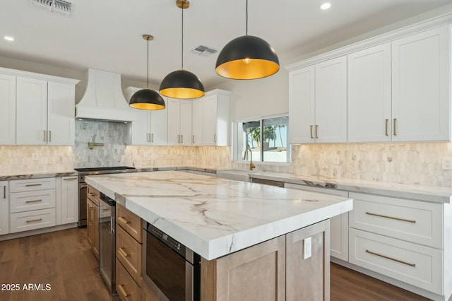 kitchen with appliances with stainless steel finishes, a center island, custom range hood, white cabinets, and decorative light fixtures