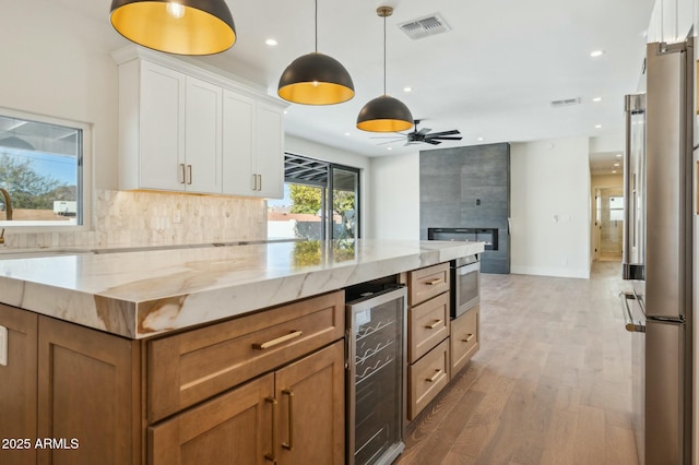 kitchen featuring a tile fireplace, white cabinets, beverage cooler, backsplash, and light stone countertops