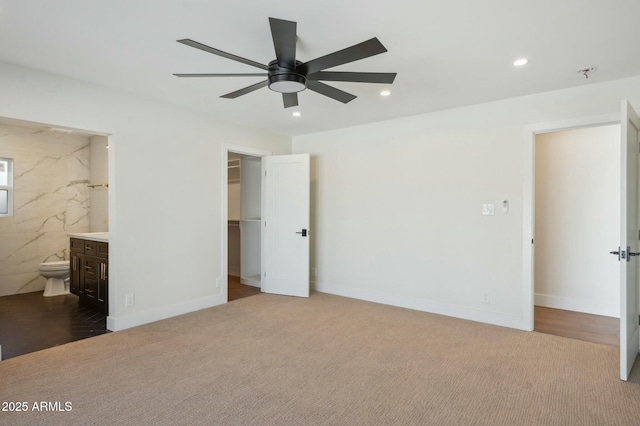 unfurnished bedroom featuring ensuite bath, a spacious closet, a closet, carpet flooring, and ceiling fan