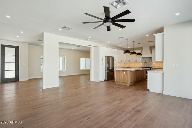 kitchen with white cabinetry, custom range hood, a spacious island, hanging light fixtures, and high end refrigerator