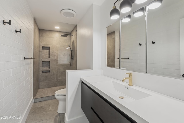 bathroom with tile patterned flooring, vanity, a tile shower, and toilet