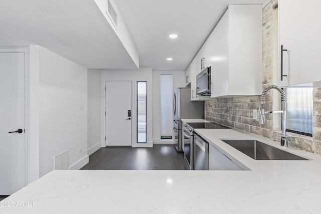 kitchen featuring sink, light stone counters, white cabinets, stainless steel appliances, and backsplash